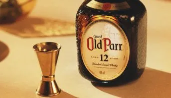 Garrafa de Old Parr 12 anos ao lado de um jigger dourado