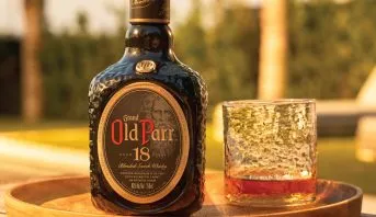 Garrafa de Old Parr 18 anos ao lado de um copo de whisky, ao ar livre