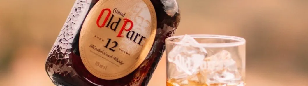 Garrafa de Old Parr 12 anos inclinada ao lado de um copo com gelo