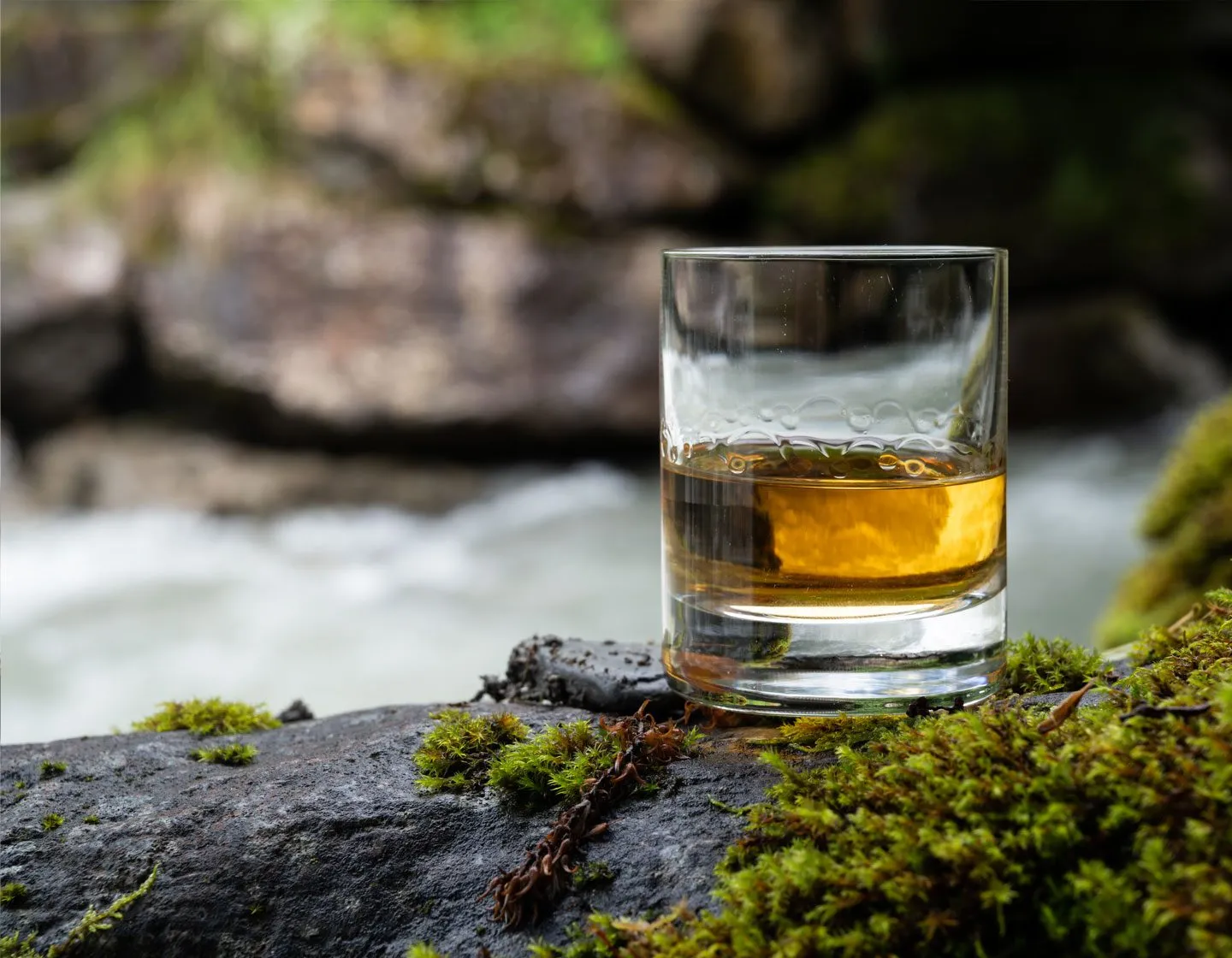 Copo baixo de whisky escocês sobre uma pedra com musgo, à beira de um rio