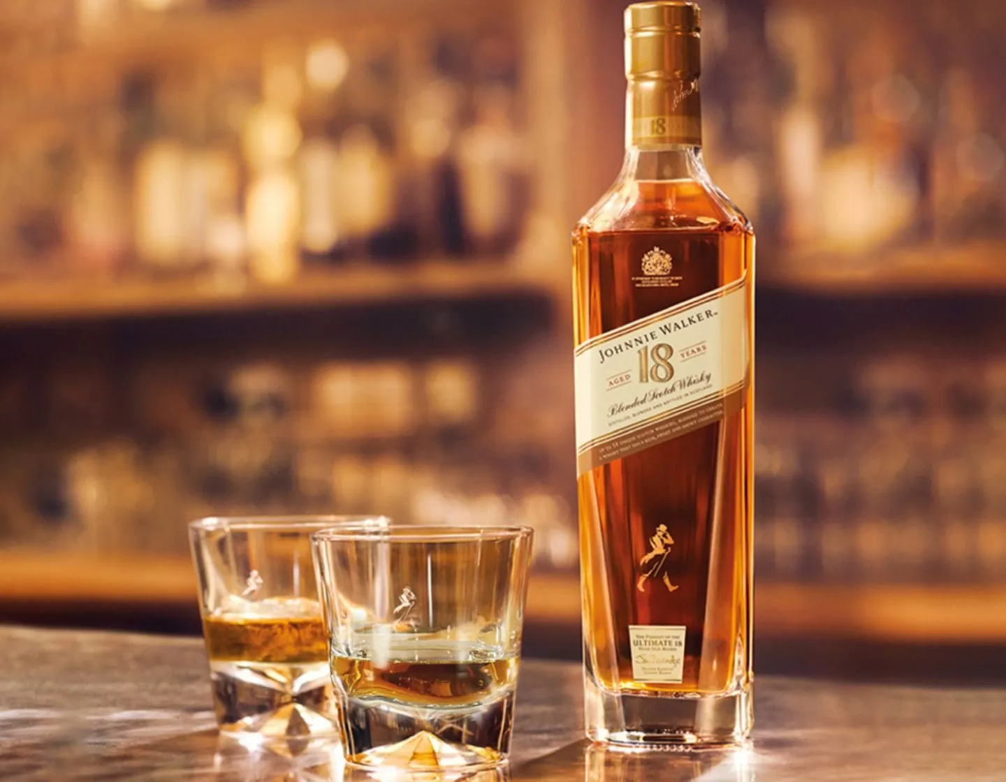 Garrafa de Johnnie Walker 18 anos ao lado de dois copos baixos, num balcão de bar