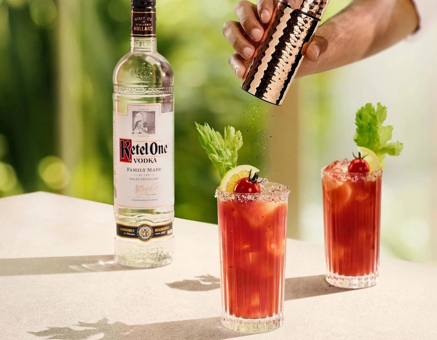Garrafa de vodka Ketel One sobre a mesa ao lado de dois coquetéis bloody mary