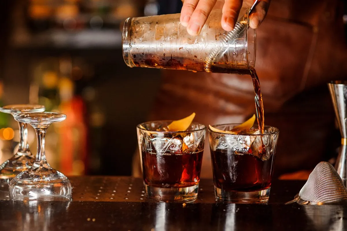 Old Fashioned sendo servido em copos com duas taças de champanhe ao lado 