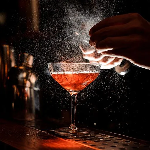 Barman’s hands sprinkling the juice into the cocktail glass 