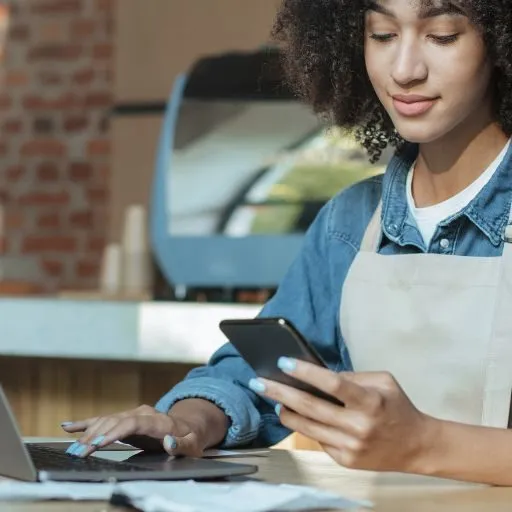 Mulher com celular e laptop usando avental de bar 