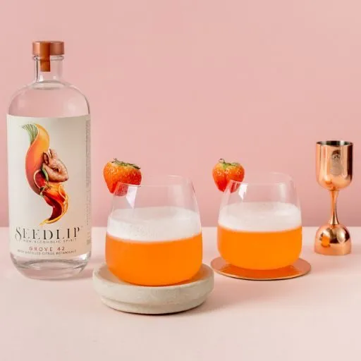 Seedlip Grove 42 com fundo rosa e dois coquetéis com guarnição de morango