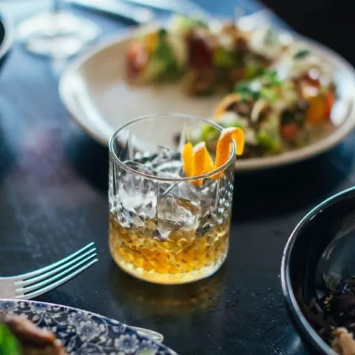   Glass of Whisky and Ice with Food Pairings on a table in a bar setting 