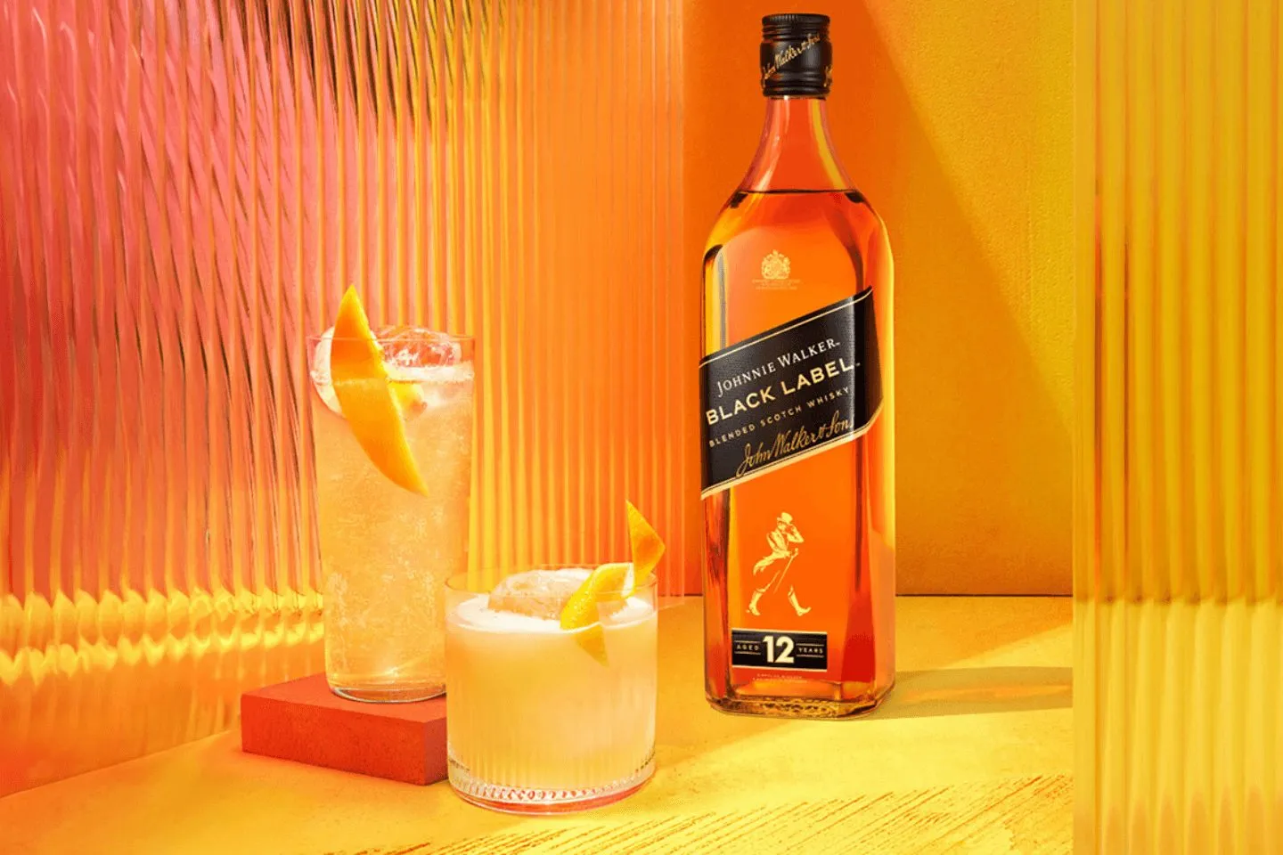 Garrafa de Johnnie Walker Black Label 12 anos com dois coquetéis de laranja num balcão amarelo